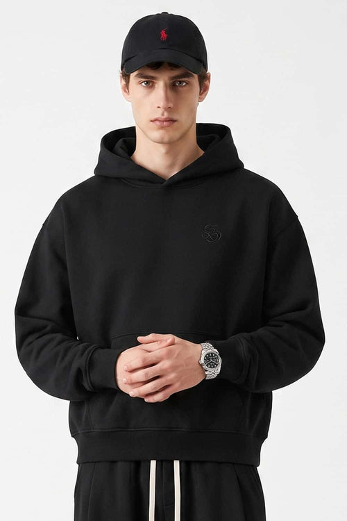Relaxed Pullover Hoodie with Embroidered Emblem in Black - front modeled view